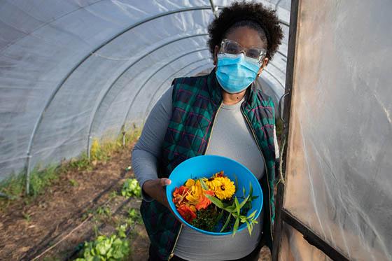 Photo of a masked Chatham University student holding a blue bowl of harvested produce, 在伊甸园大厅校园的温室入口处
