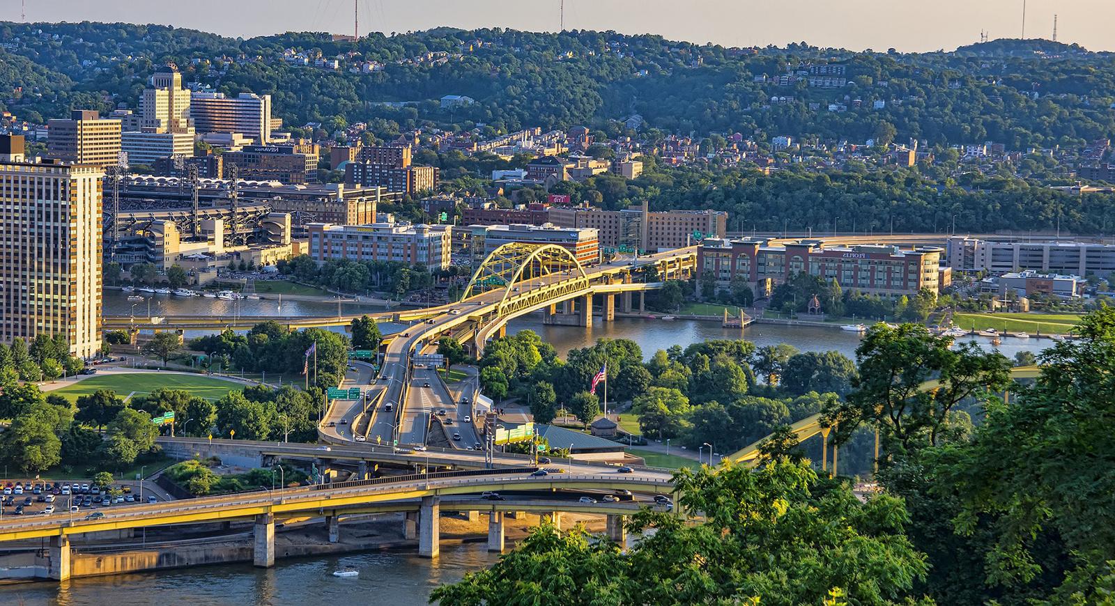 Photo of Pittsburgh's yellow bridges 和 rolling hills framing rivers at sunset. 