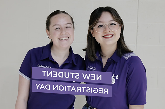 Two student volunteers wearing purple smile together for a photo. '新生注册日' is written on a purple banner in front of them.