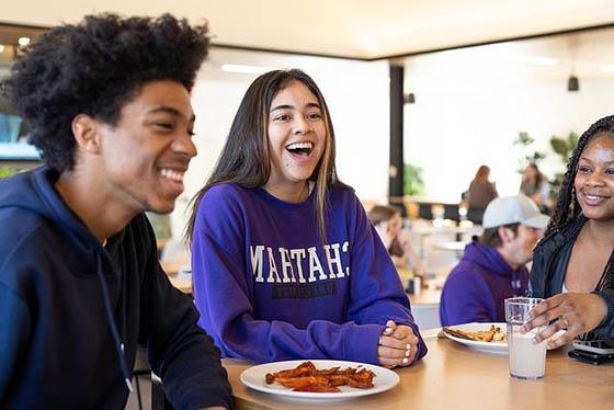 A group of three students smile 和 laugh at a dining hall table