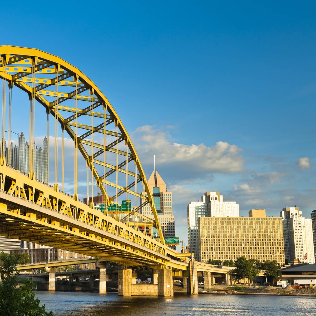 Photo of a yellow bridge over a river 和 Pittsburgh skyline